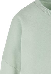 Pull vert clair à col rond montrant l'épaule et le haut de la manche avec une texture tricotée visible et un col côtelé.