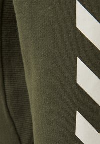 Olivgrön tyg har en slät textur med vertikala ribbor och vita diagonala ränder som en märkbar designdetalj.