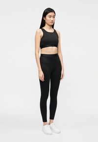 Sujetador deportivo negro y leggings de talle alto en una tela suave y elástica. Presenta un logo sutil en la cintura; combinado con zapatillas blancas.