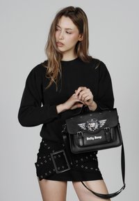 Bolso tipo satchel negro de cuero sintético con diseño de Betty Boop, acentos de alas plateadas, doble hebilla y correa de hombro ajustable.
