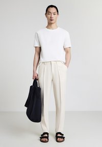 Maglietta bianca a girocollo, pantaloni a pieghe color crema, borsa a tracolla nera e sandali neri con cinturini. Tessuto liscio, vestibilità comoda, texture leggera.