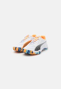 Weiße Sportschuhe mit einem orange-schwarzen Design, strukturiertem Mesh-Obermaterial und einer mehrfarbigen Gummisohle mit Zickzackmustern.
