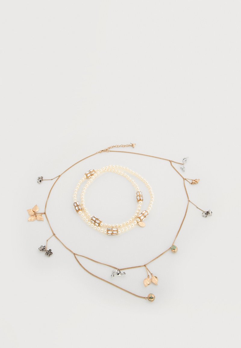 Τρία στρώματα με κολιέ που διαθέτο υν μαργαριταρένιες χάντρες, χρυσές μεταλλικές λεπτομέρειες και φυλλαράκια σε διάφορα φινιρίσματα, τοποθετημένα σε ανοιχτό φόντο.