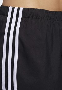 Pantalones cortos deportivos negros con una cintura elástica, que presentan tres rayas verticales blancas en el costado para un contraste y un detalle de textura.