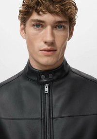 Czarna skórzana kurtka z wysokim kołnierzem, ozdobiona srebrnym zamkiem błyskawicznym i guzikami, o gładkiej fakturze i dopasowanym kroju.