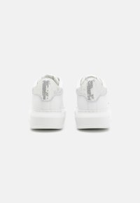 Vita sneakers med en slät läderöverdela, texturerade silverfärgade hälflikar, rund tå och en tjock vit sula. Minimalistisk design.