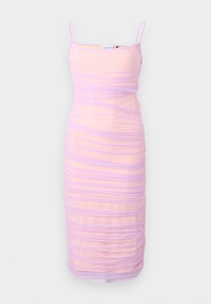 Žena s tmavými vlasmi a tetovaniami, oblečená v priliehavých, riasených, svetlofialových midi šatách bez rukávov a béžových sandáloch na vysokom podpätku.