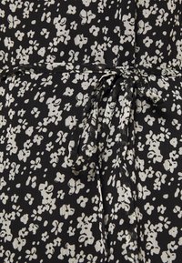 Tissu noir avec un motif floral blanc, doté d'une ceinture nouée. La texture semble légère et légèrement froissée.