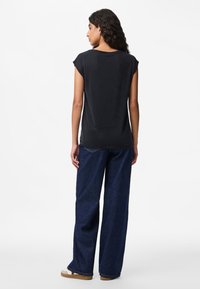 Juodas trumpomis rankovėmis laisvo stiliaus viršus. Derinama su laisvomis mėlynomis džinsinėmis kelnėmis ir kasdieniškais smėlio spalvos batais. Lygus paviršius, minimalistinis dizainas.