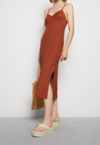 Ruskivärinen ribbimidi mekko ohuilla olkaimilla ja sivurei'illä, yhdistettynä kevyisiin platform-sandaaleihin ja kudottuun kassi.