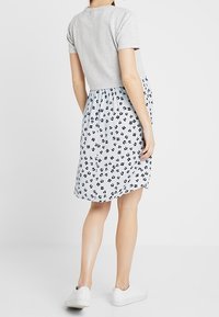 Un haut gris à manches courtes associé à une jupe bleue ornée de motifs floraux blancs et noirs. Des baskets blanches complètent l'ensemble.