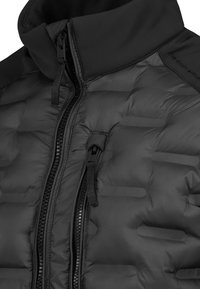 Schwarze gepolsterte Jacke im Detail, die das Doppelreißverschluss-Design und den hohen Kragen mit Stoffziehbändern an den Reißverschlüssen zeigt.