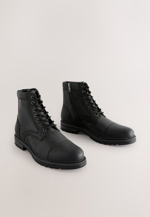 Stivaletti neri in pelle con chiusura frontale con lacci, cerniera laterale, punta rinforzata e suola testurizzata per una migliore aderenza.