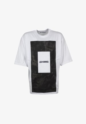 Maglietta bianca oversize con una grande stampa rettangolare nera e il testo "LES HOMMES" centrato in un rettangolo bianco più piccolo.