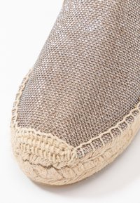 Espadrille-schoen met een metallic bruin geweven bovenwerk, ronde neus en een natuurlijke jute zool met een gevlochten accent langs de rand.