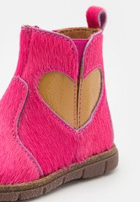 Botte à cheville en fourrure rose avec une découpe en forme de cœur, des accents en cuir marron, des coutures contrastées et une semelle en caoutchouc texturé.