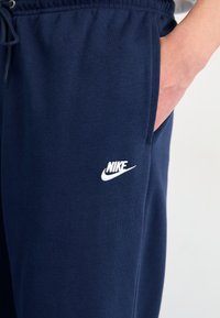 Tumši zili Nike sporta bikses kokvilnas maisījumā, ar elastīgu jostu un auklu, sānu kabatām un baltu logotipu kreisajā augšstilbā.