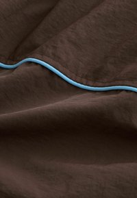 Tissu marron avec des surpiqûres visibles et une couture ondulée soulignée par un fin passepoil bleu clair.