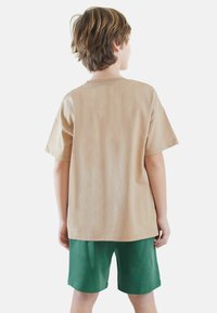 Beige bomulds T-shirt med kortermer, afslappet fit, parret med grønne shorts. T-shirten har et simpelt design uden mønstre eller dekorationer.
