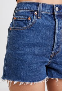 Denimshorts med fransad fåll, mellanmörk blå tvätt, koppardetaljer, femfickdesign och kontrasterande orange sömmar.