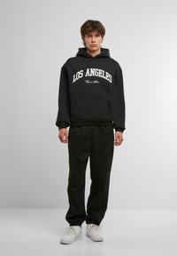 Czarna bluza z kapturem z napisem "LOS ANGELES" w białym kolorze, w połączeniu z czarnymi dresami. Oba elementy wykonane są z miękkiego, teksturowanego materiału. Białe sneakersy dopełniają całość.