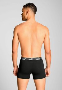 Black boxer briefs made of smooth fabric with a wide elastic waistband featuring the Puma logo in white. Showing a fitted design from the back.