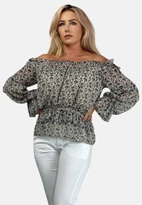 Kwiatowa bluzka bez ramiączek z przezroczystego materiału, z falbaniastymi mankietami i w talii, w lekkiej kolorystyce bieli, beżu i ciemnego wzoru.