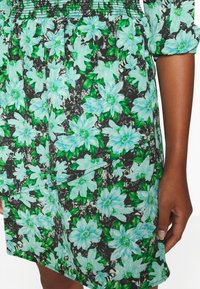 Vestido de tela negra con un vibrante estampado floral en azul claro y verde. Cuerpo texturizado con detalles fruncidos y un dobladillo asimétrico.