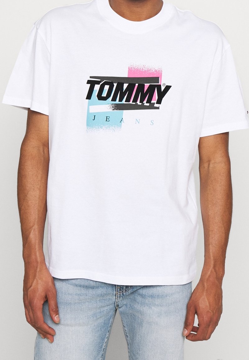 Camiseta de algodón blanca con un logo gráfico en negro, rosa y azul, con un corte relajado y cuello redondo.