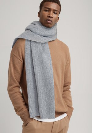 Gray knit scarf worn over a brown sweater, featuring a ribbed texture and long length, draping elegantly around the neck.