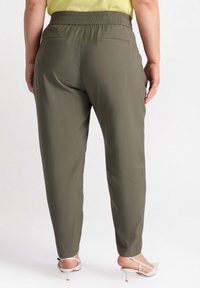 Olive green trousers with a relaxed fit, elastic waistband, two back pockets, and tapered legs, paired with light-colored heels.