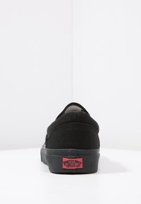 Baskets noires en toile avec un design bas, bout rond et semelle en caoutchouc noire. Présente un logo rouge "Off the Wall" au dos.