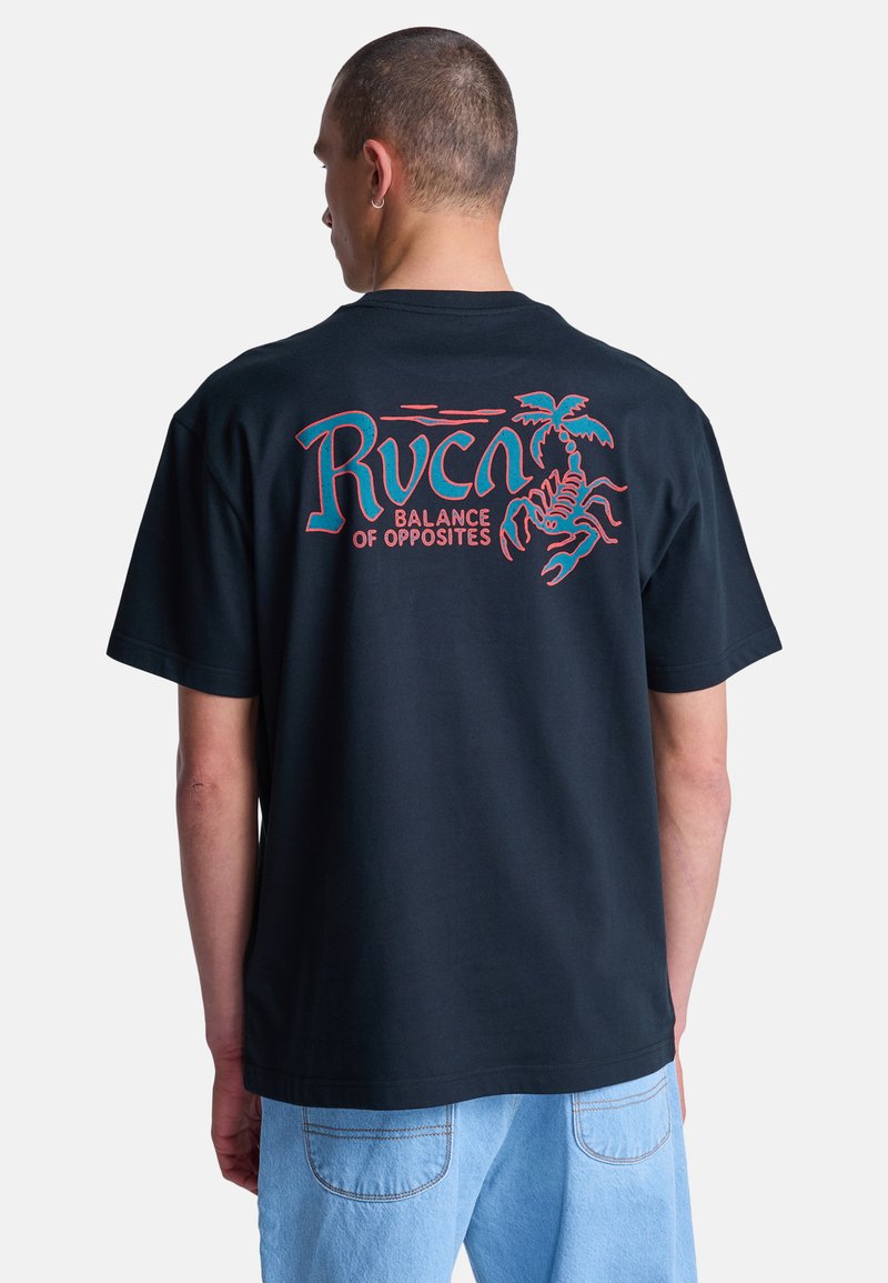 Hombre con camiseta negra con texto rojo y azul "Rvca Balance of Opposites" y gráfico de escorpión, combinado con jeans azul claro, de espaldas.