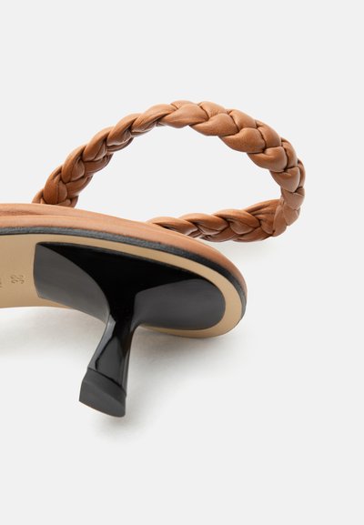 Καφετί πλεκτό δερμάτινο σανδάλι με μαύρο χαμηλό τακούνι, εμφανισμένο από την πλευρά της σόλας σε λευκό φόντο.