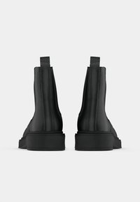 Pari mustia nahkaisia nilkkasaappaita vetonauhoilla, nähtynä takaa valkoista taustaa vasten.