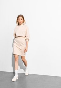 Beige Kapuzenpullover kombiniert mit einem engen beigen Rock. Glatte Textur, lockere Passform und weiße Sneaker mit strukturierten Sohlen. Minimalistisches Design.