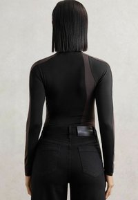 Body negru cu mâneci lungi, cu panouri contrastante, textură netedă, croială ajustată, asortat cu blugi negri cu talie înaltă, având buzunare la spate.