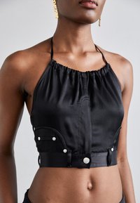 Čierny halter crop top so zhrnutým výstrihom, saténovou textúrou, dekoratívnymi striebornými gombíkmi a bočnými vreckami s zakrivenými švami.