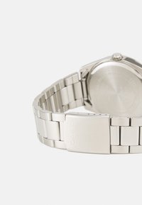 Orologio in acciaio inossidabile con finitura argento metallico, caratterizzato da un design a bracciale collegato e una chiusura contrassegnata con "CASIO". Cassa circolare sul retro.