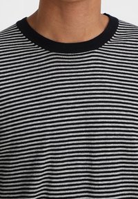 T-shirt a righe bianche e nere con design a collo rotondo. Il tessuto appare morbido, con una texture liscia e linee orizzontali uniformi.