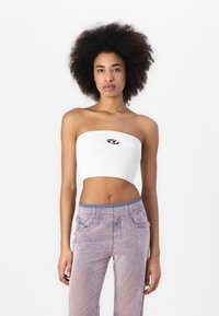 Bílé žebrované krátké bandeau top s centrálním logem, spárované se světle růžovými širokými kalhotami s texturou.