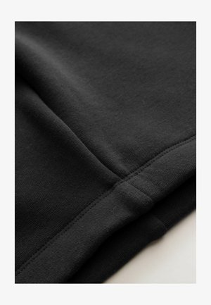 Tela negra con una textura suave, que presenta costuras cosidas y un ligero estiramiento. El diseño es simple y minimalista.