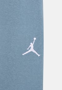 Tejido de algodón azul claro con un logotipo Jumpman bordado en blanco, que representa una figura en el aire, con un acabado texturizado.