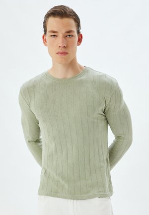 Camisa de punto de manga larga en un verde claro, con un patrón texturizado, escote redondo y diseño ajustado, que destaca líneas verticales sutiles y detalles de punto abierto.