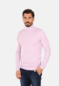 Maglione a collo alto di un viola chiaro, realizzato in tessuto morbido. Presenta maniche lunghe e orlo a coste. Indossato con jeans in denim scuro.
