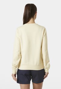 Sudadera amarilla claro con cuello redondo, puños y bajo de canalé. La parte trasera es lisa y sin adornos. Combinada con pantalones cortos azul marino.