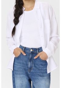 Valkoinen pellavapaita, joka on napitettu auki valkoisen ribatun topin päällä, yhdessä korkeavyötäröisten sinisten farkkujen kanssa. Asu on rento ja mukava.