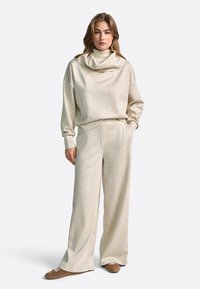Set de lounge bej, compus dintr-un pulover cu guler tip cowl, cu o croială lejeră, și pantaloni largi dintr-un material moale și texturat. Design minimalist.