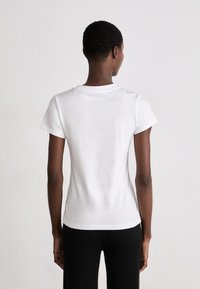 T-shirt bianco in cotone con maniche corte e scollatura rotonda, mostrato dal retro, che mette in risalto una silhouette aderente e una trama liscia.