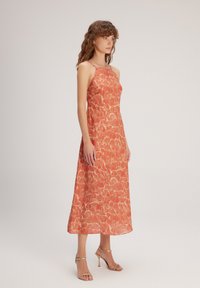 Oranges Midi-Kleid mit Blumenmuster, Spaghettiträgern und fließender Silhouette. Leichter Stoff mit glatter Textur. Goldene Sandalen.
